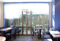 浦和区 Fruit Parfaiteria Kaju の店内。青いタイルと椅子、大きな窓から見えるテラス席（または庭）。明るく開放的な雰囲気。