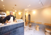 壹尺珈琲（イチシャクコーヒー）の店内。紺色のタイル張りのカウンターに立つ店主と、壁沿いに設けられた木製スツールとベンチのシンプルなイートインスペース。