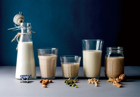 「MILK STAND BY COFFEE MILK」の多様なミルクのラインナップ。左からミルクボトル、アーモンド、ピスタチオ、大豆（ソイ）、くるみのミルクが入ったグラスが並び、手前にはそれぞれの原材料が添えられている。